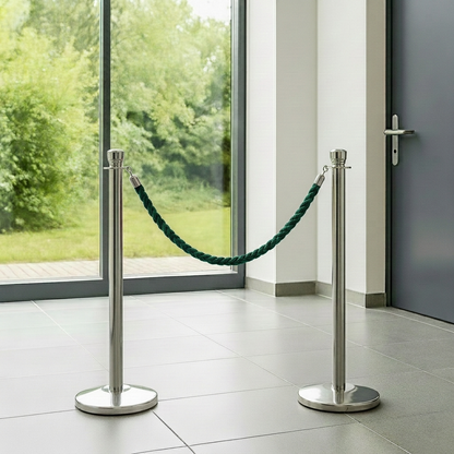 Two silver stanchions with green rope in front of a glass door with a view of greenery outside.